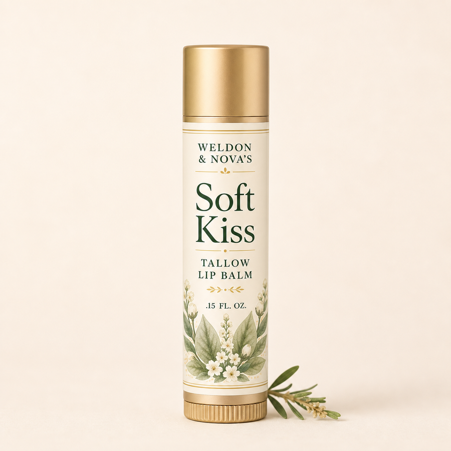 Weldon & Nova's Soft Kiss Tallow Lip Balm in a cylindrical white and gold tube with botanical illustrations, set against a solid cream background with a sprig of green leaves at its base.